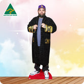 Cardboard cutout of a person wearing a black coat with gold accents and a purple cap, on a wooden floor with a colorful gradient background.
