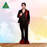 Man in a black suit with red lining standing on a red carpet with a colorful gradient background.