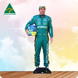 Person in green racing suit holding a helmet with 'Aston Martin' branding on a wooden floor.