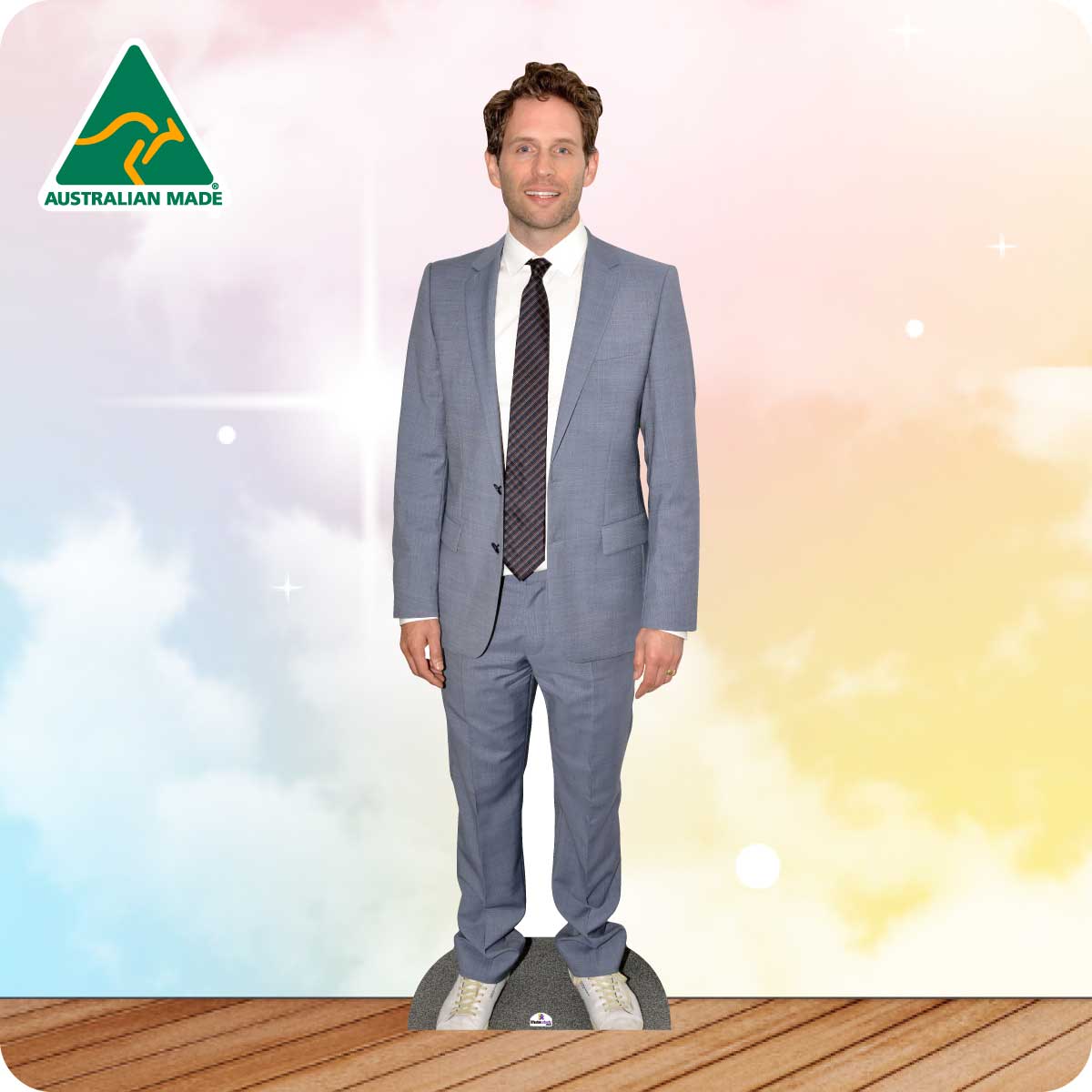 Man wearing a gray suit with a tie against a colorful background with 'Australian Made' logo.