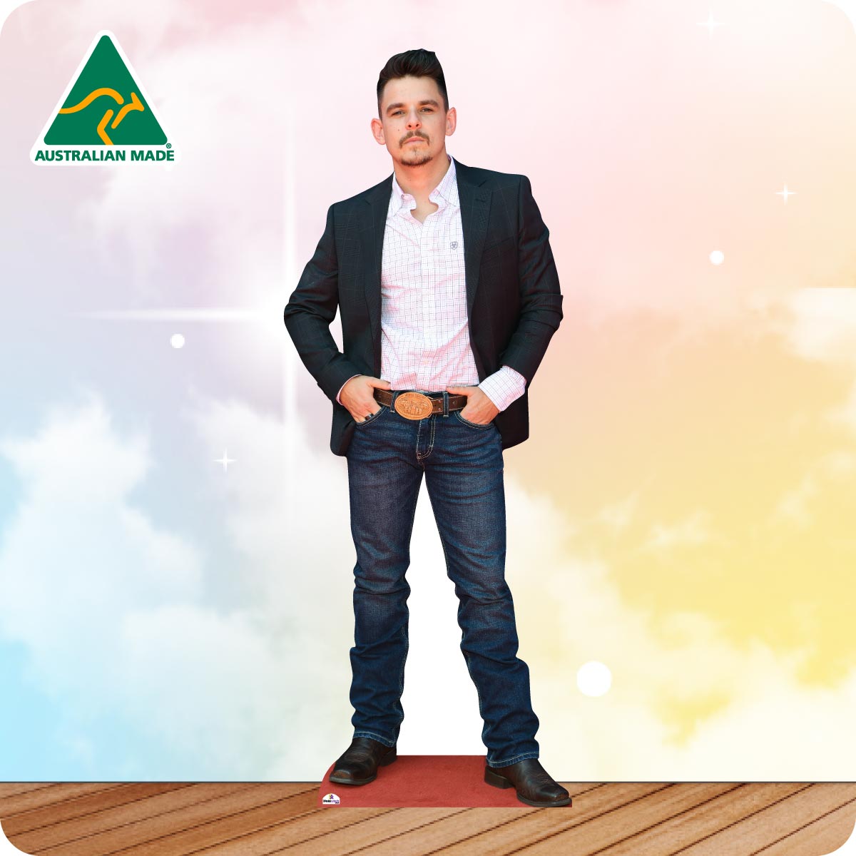 A man modeling a dark blazer, white checkered shirt, and blue jeans with a large brown belt, standing on a wooden floor against a pastel sky background. An 'AUSTRALIAN MADE' logo is visible in the top left corner.