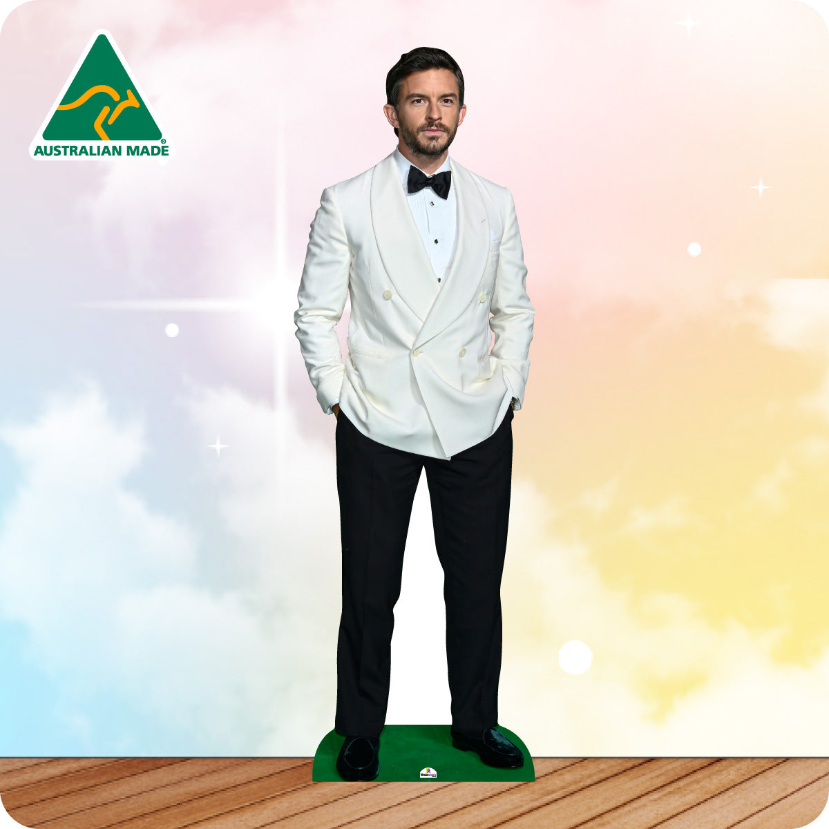 Cardboard standee of a man in a white tuxedo with a black bow tie on a wooden floor.