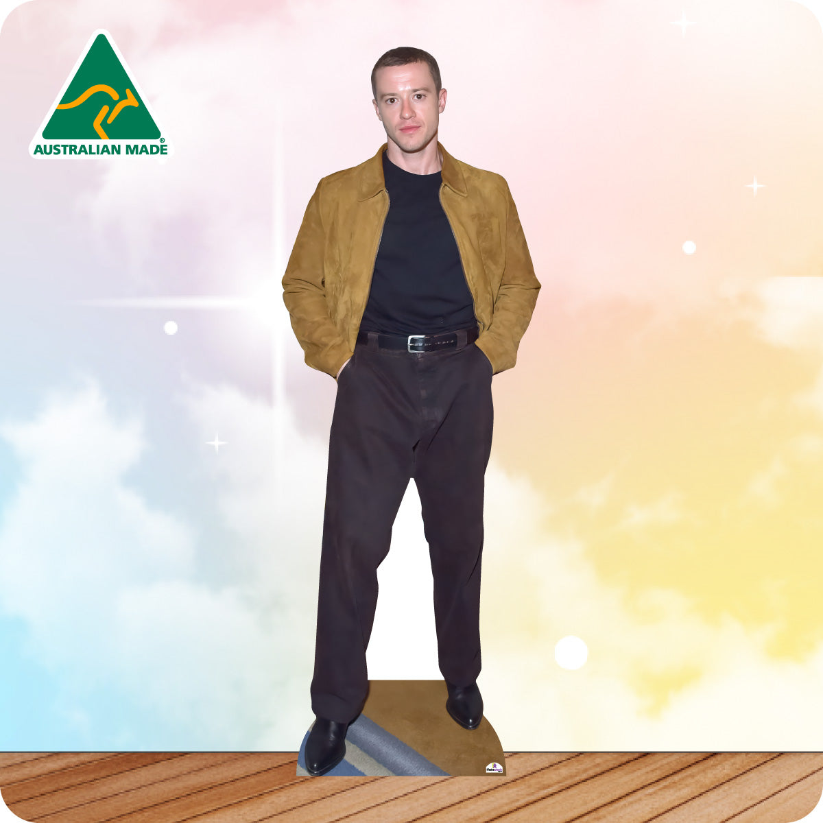 Man wearing a tan jacket and dark pants standing on a wooden floor with a colorful gradient background.