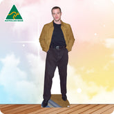 Man wearing a tan jacket and dark pants standing on a wooden floor with a colorful gradient background.