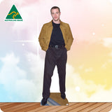 Man wearing a tan jacket and dark pants standing on a wooden floor with a colorful gradient background.
