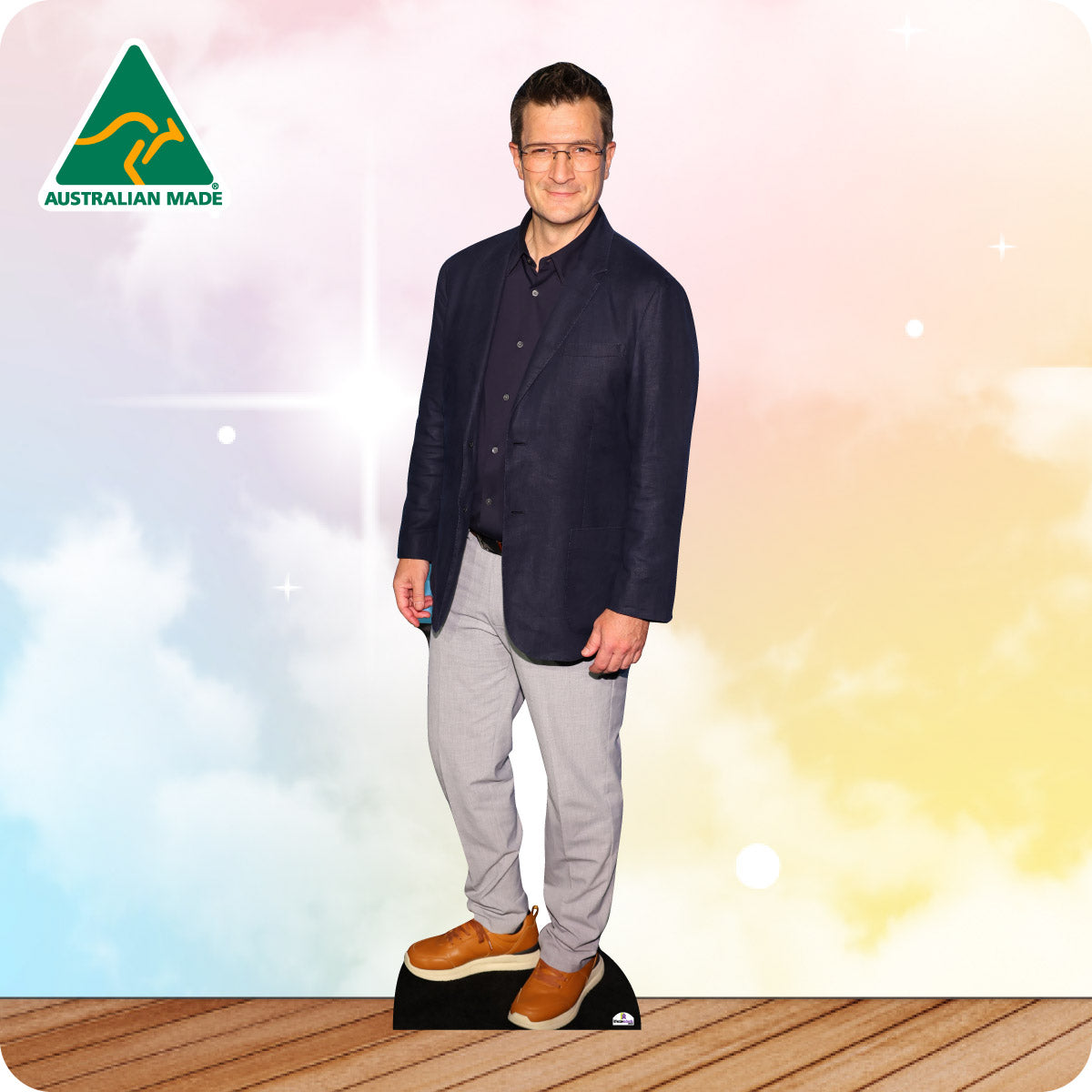 Man wearing a navy jacket and gray pants standing on a wooden floor with a colorful background and 'Australian Made' logo.