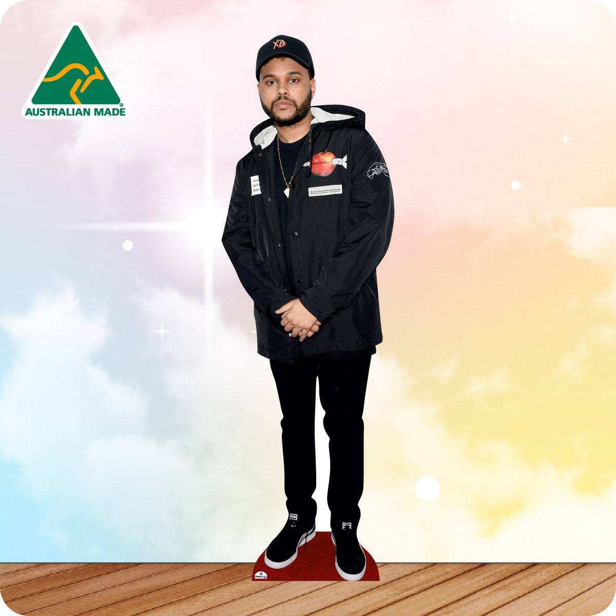 Cardboard cutout of a person wearing a black jacket with logos, standing on a wooden floor with a colorful gradient background.