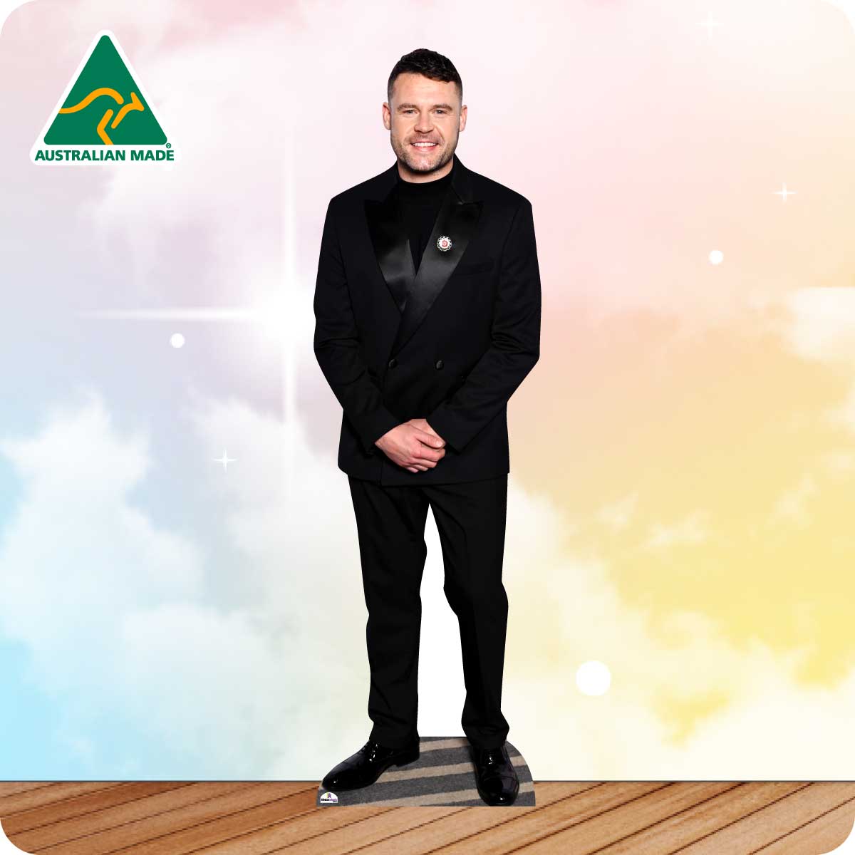 Man in a black suit standing on a wooden floor with a colorful background and 'Australian Made' logo.
