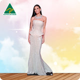 Woman in a sparkly silver evening gown on a wooden floor with a colorful, blurred background.