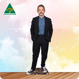 Man in a black suit with a blue shirt and patterned shoes standing on a wooden floor with a colorful gradient background.