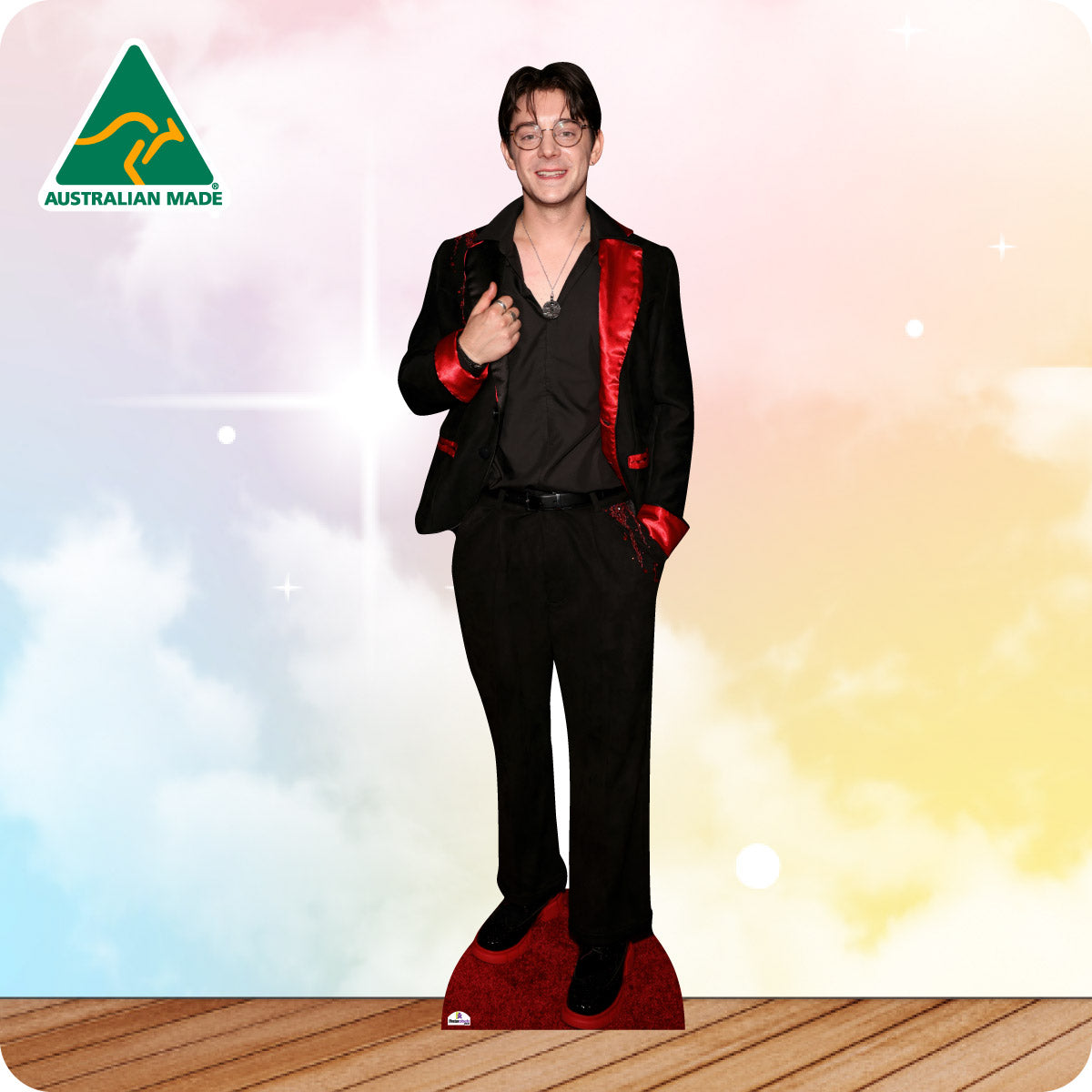 Man in a black suit with red lining standing on a red carpet with a colorful gradient background.
