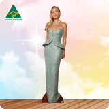 Woman in a sparkly green dress standing on a wooden floor with a colorful background