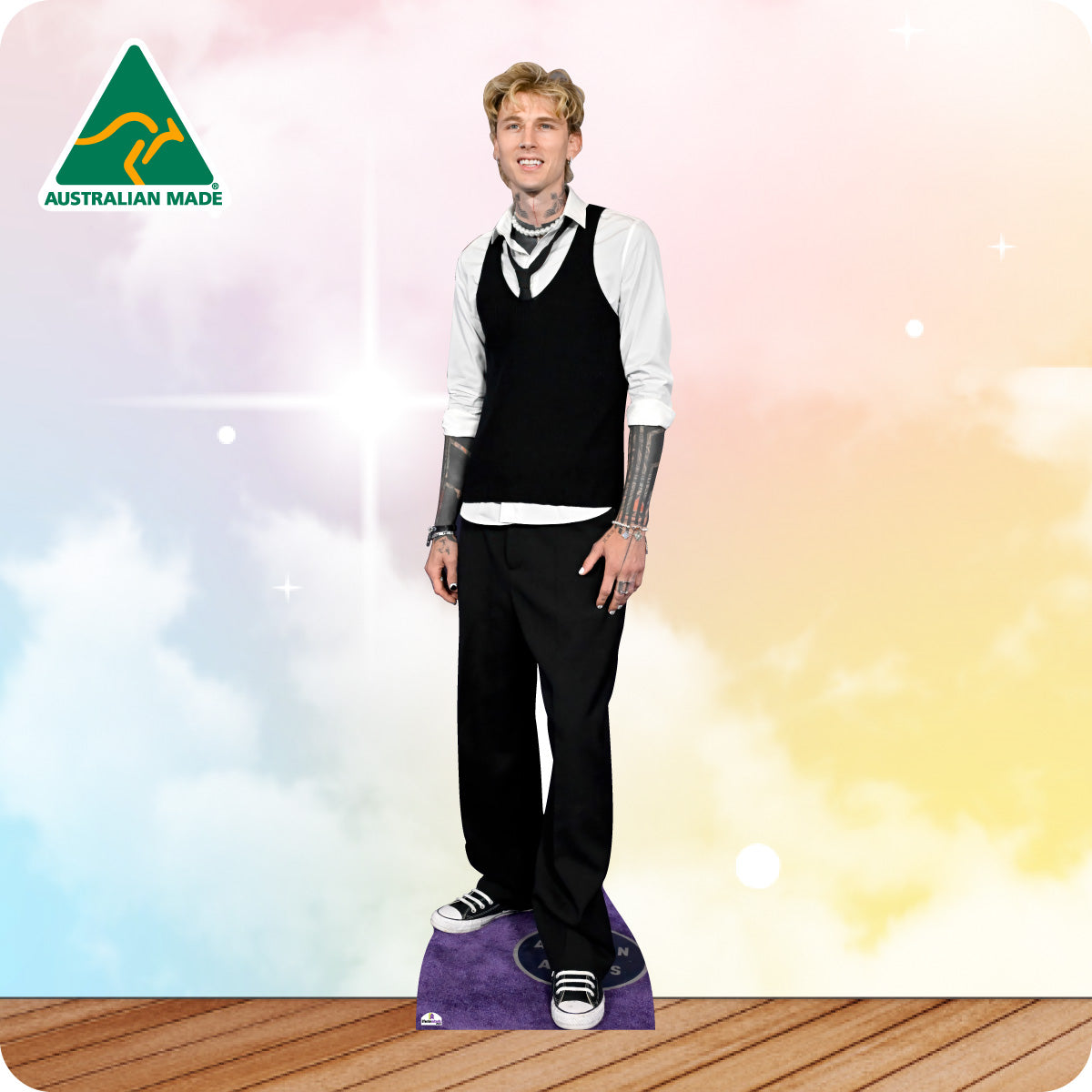 Cardboard cutout of a person wearing a black vest and pants with a white shirt, standing on a wooden floor with a colorful gradient background.